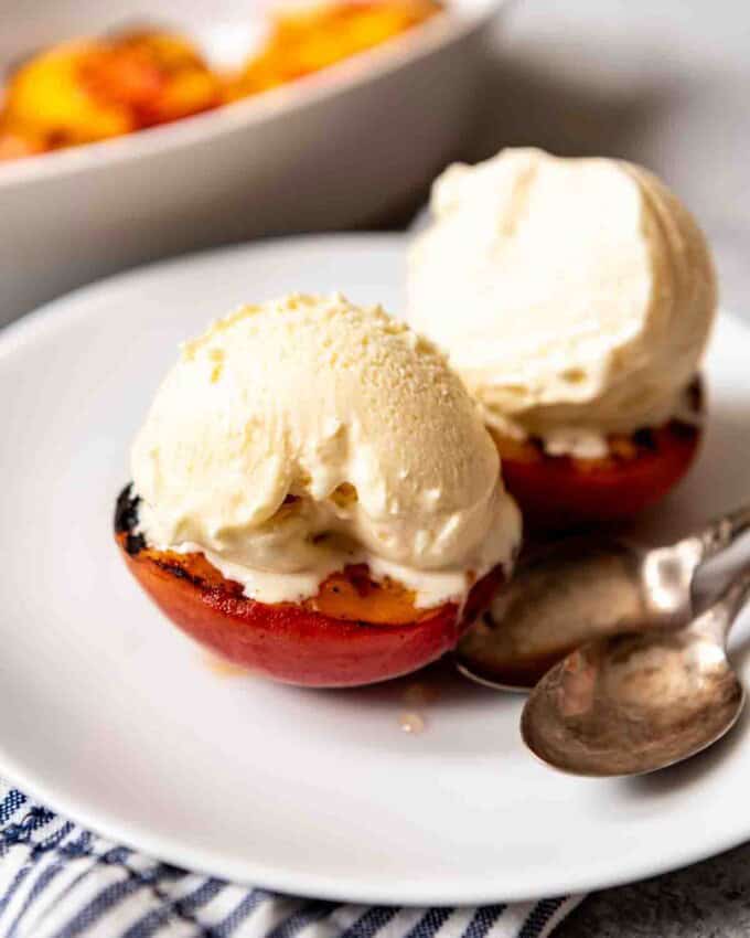 A plate with two spoons and two peaches with ice cream.