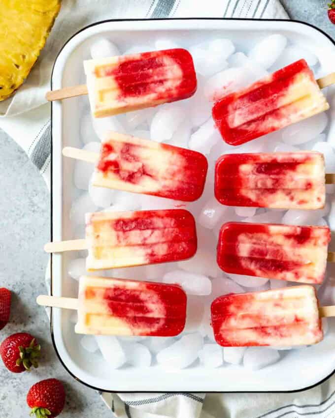 a baking dish full of ice topped wth fresh strawberries and strawberry pineapple coconut swirl popsicles