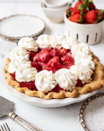 A fresh strawberry pie in front of a container of strawberries.