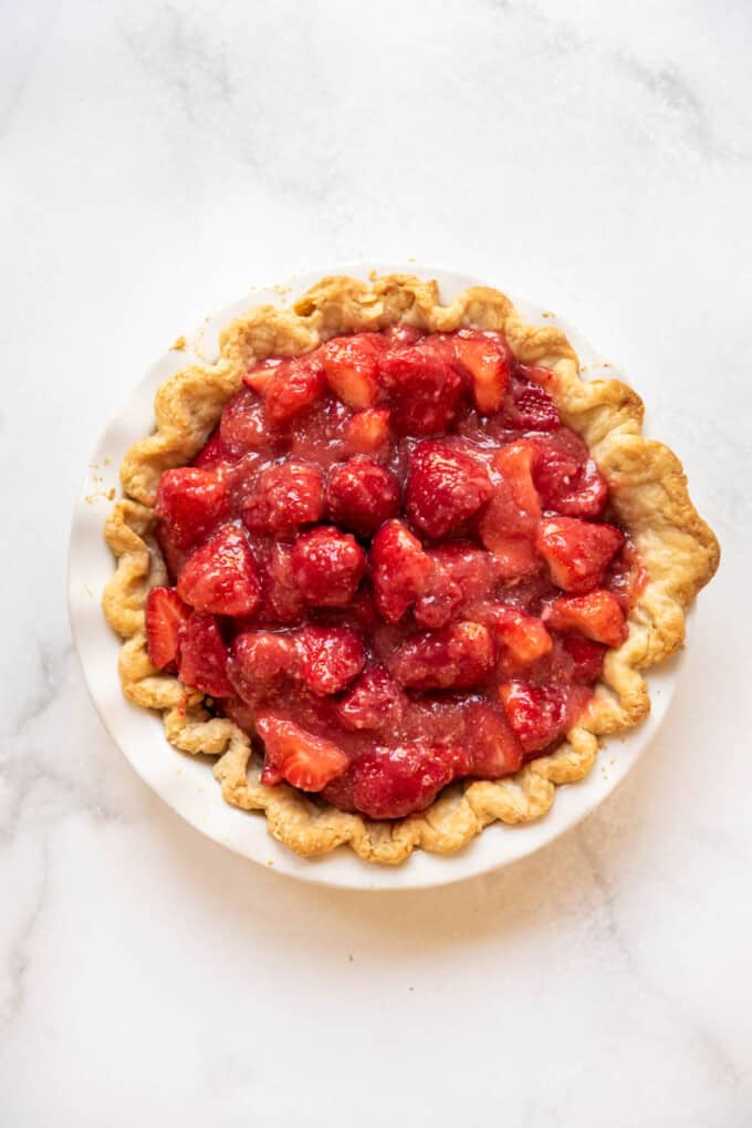 Adding glazed strawberry pie filling to a baked pie crust shell.