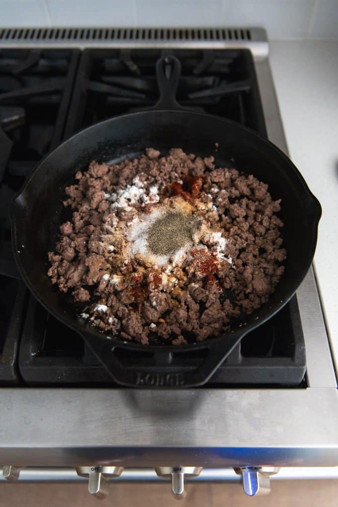 An image of spices sprinkled over browned ground beef.