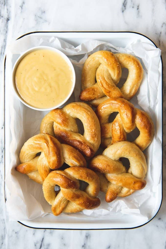 An image of some homemade soft pretzels stacked in a dish with a bowl of mustard cheese dipping sauce on the side.