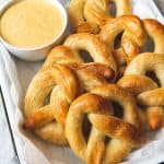 a baking dish filled with golden pretzels and a bowl of mustard cheese dip