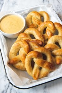 a baking dish filled with golden pretzels and a bowl of mustard cheese dip
