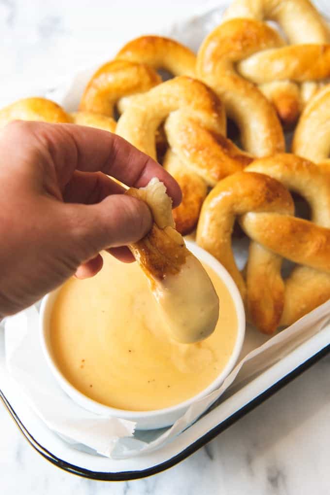 dipping a piece of pretzel in mustard cheese sauce