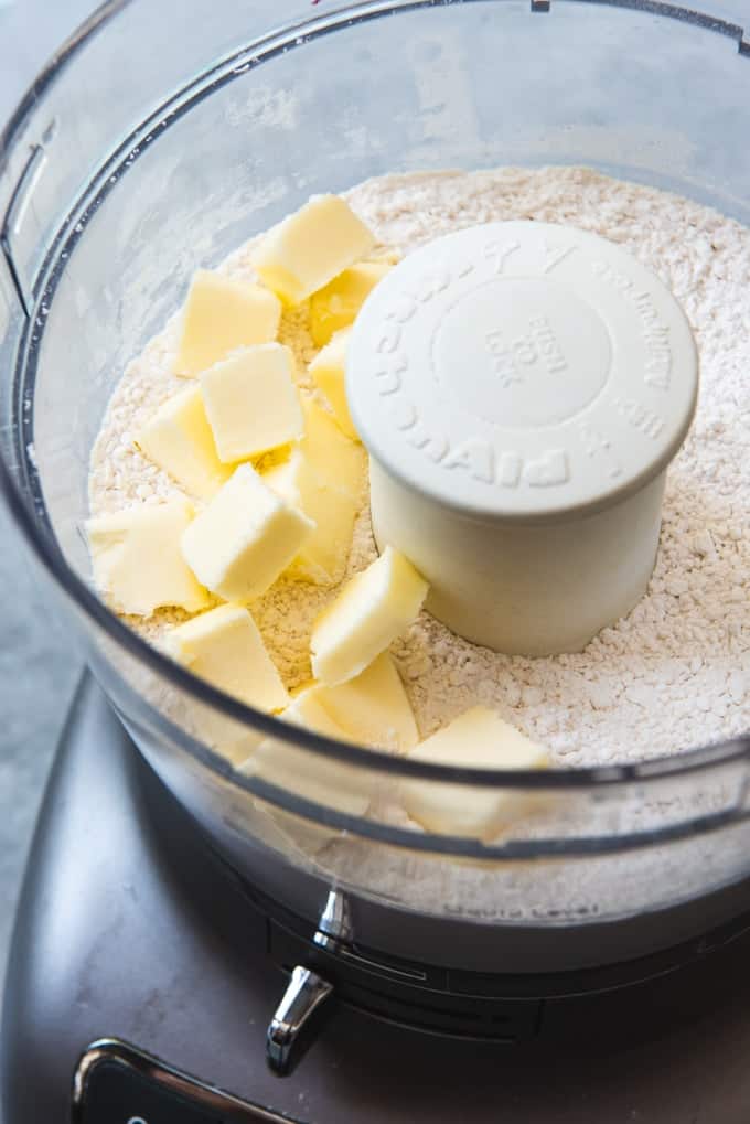 An image of cubed cold butter in a food dprocessor with flour, baking powder, and salt for making homemade buttermilk biscuits from scratch.