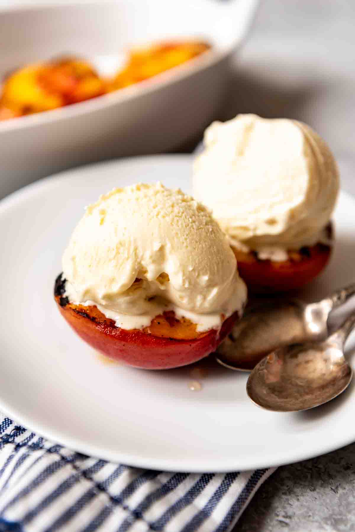 A plate with two spoons and two peaches with ice cream.