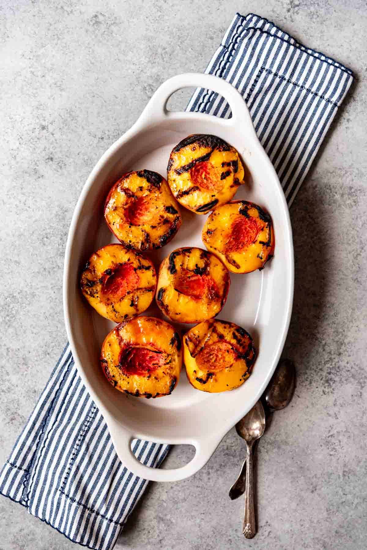 An aerial view of a white baking dish with 7 grilled peach halves inside.