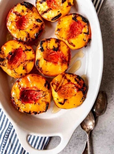 An image of a dish full of grilled peaches drizzled with honey.