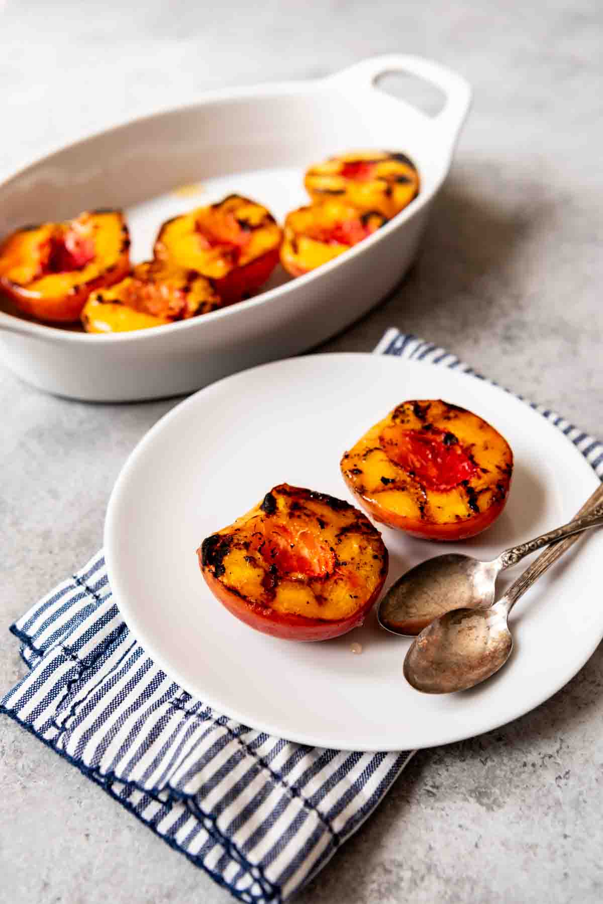 Two grilled peaches on a white plate.