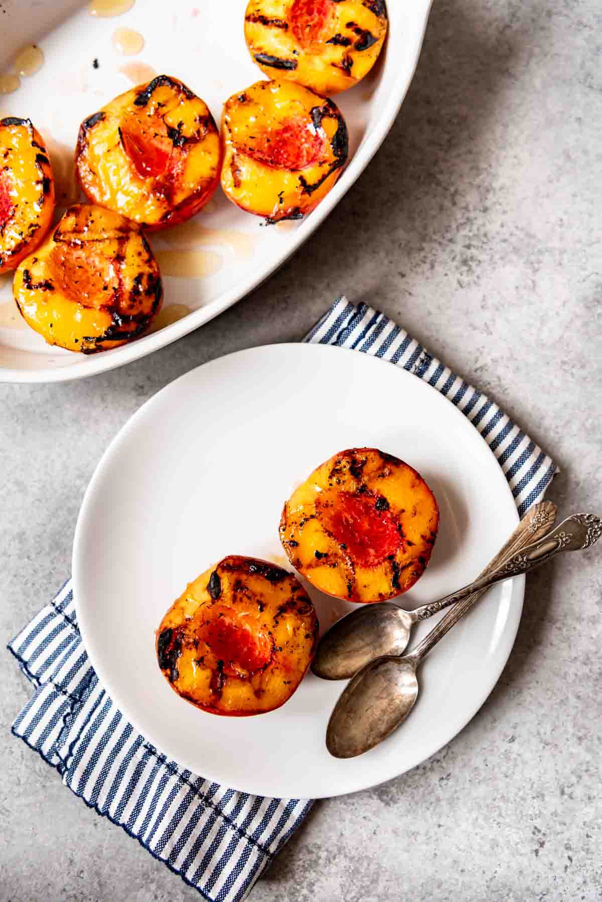 An image of two grilled peach halves on a white plate, drizzled with honey.