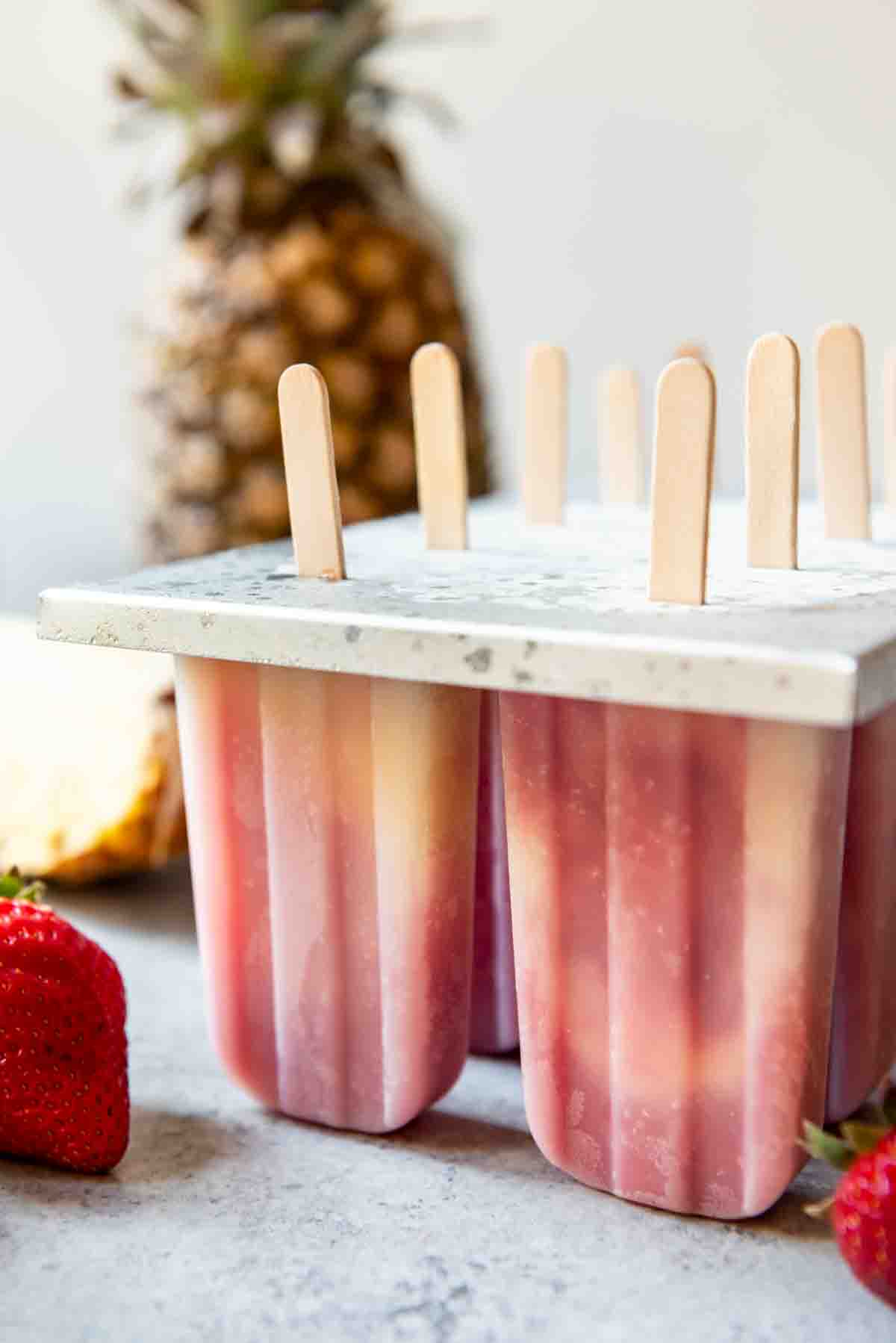 An image of pineapple strawberry coconut popsicles in a popsicle mold right out of the freezer.