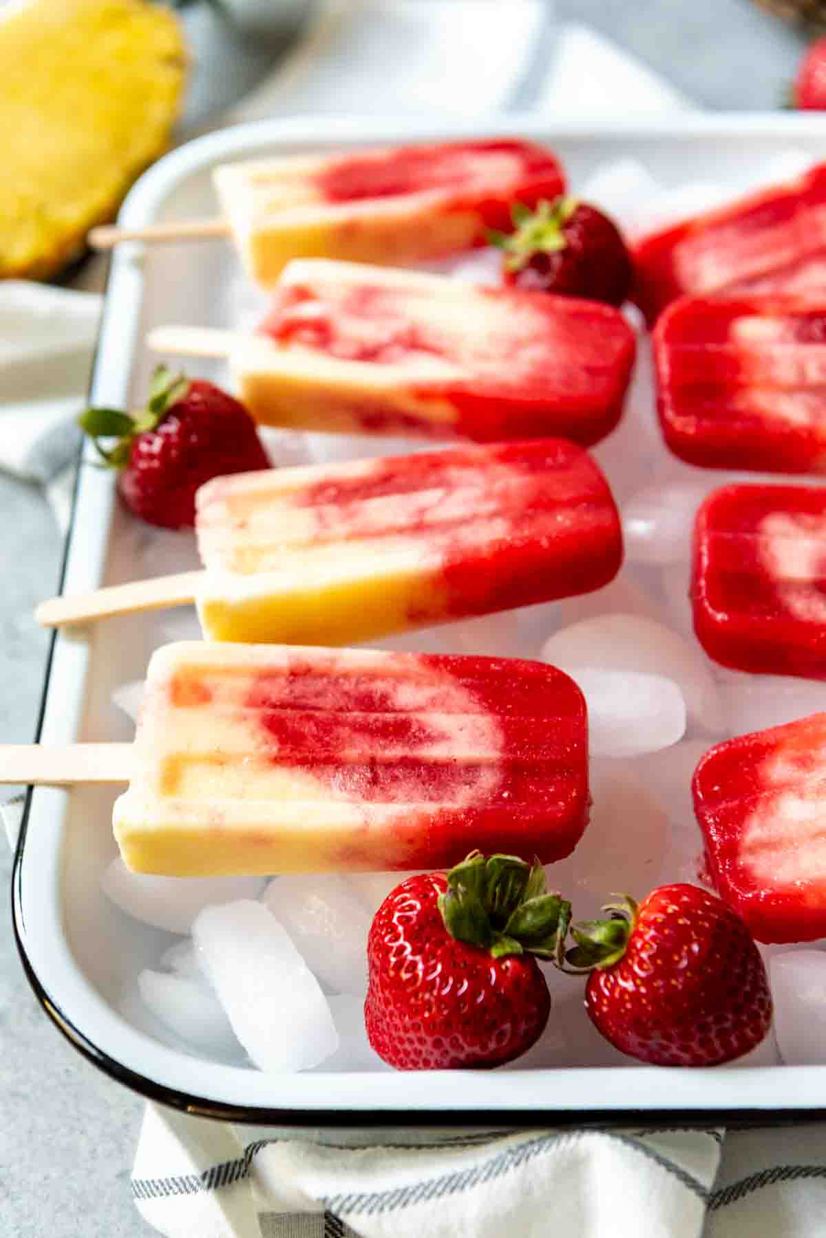 An image of a white pan with ice cubes and non alcoholic lava flow popsicles on top.