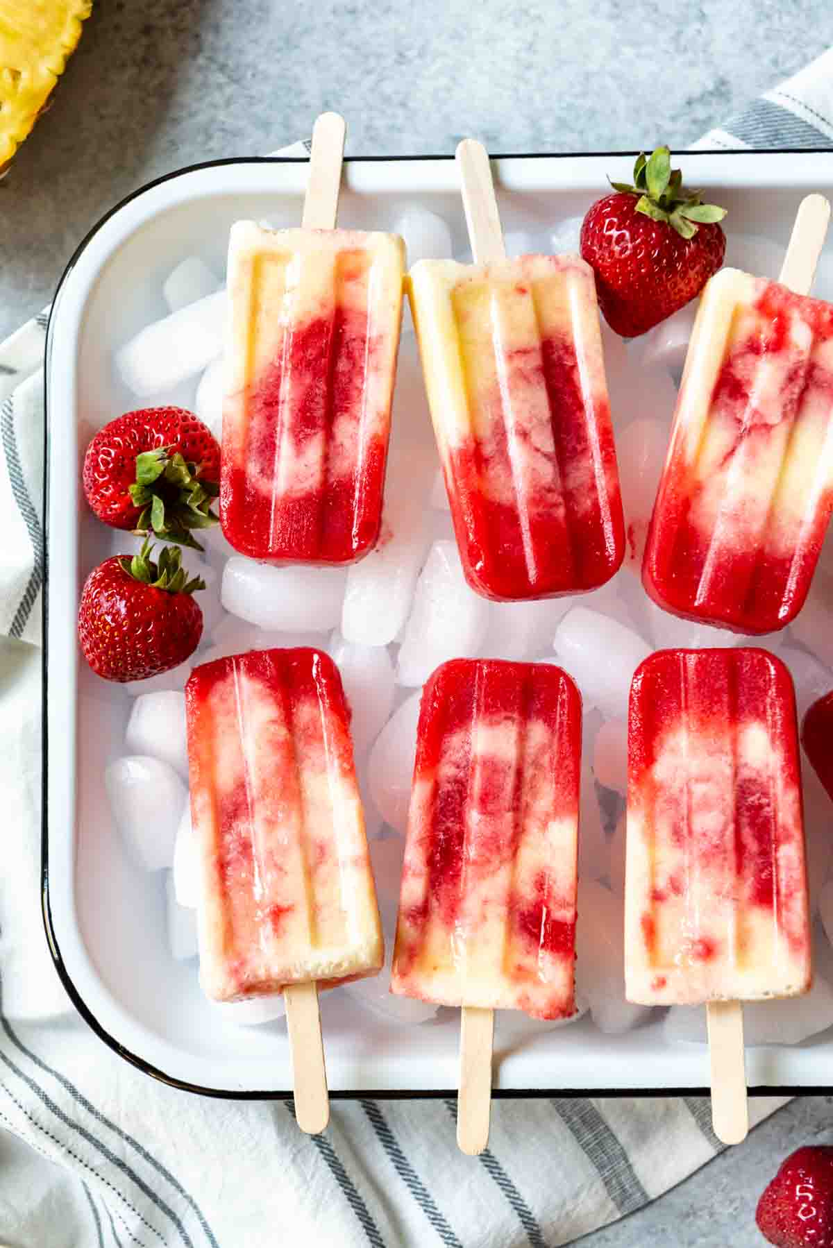 a baking dish full of ice topped wth fresh strawberries and strawberry pineapple coconut swirl popsicles