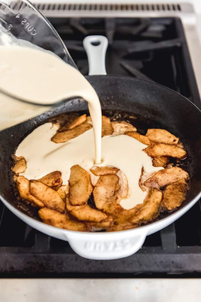 An image of German pancake batter being poured into a skillet of sauteed cinnamon apples for a German apple pancake recipe.