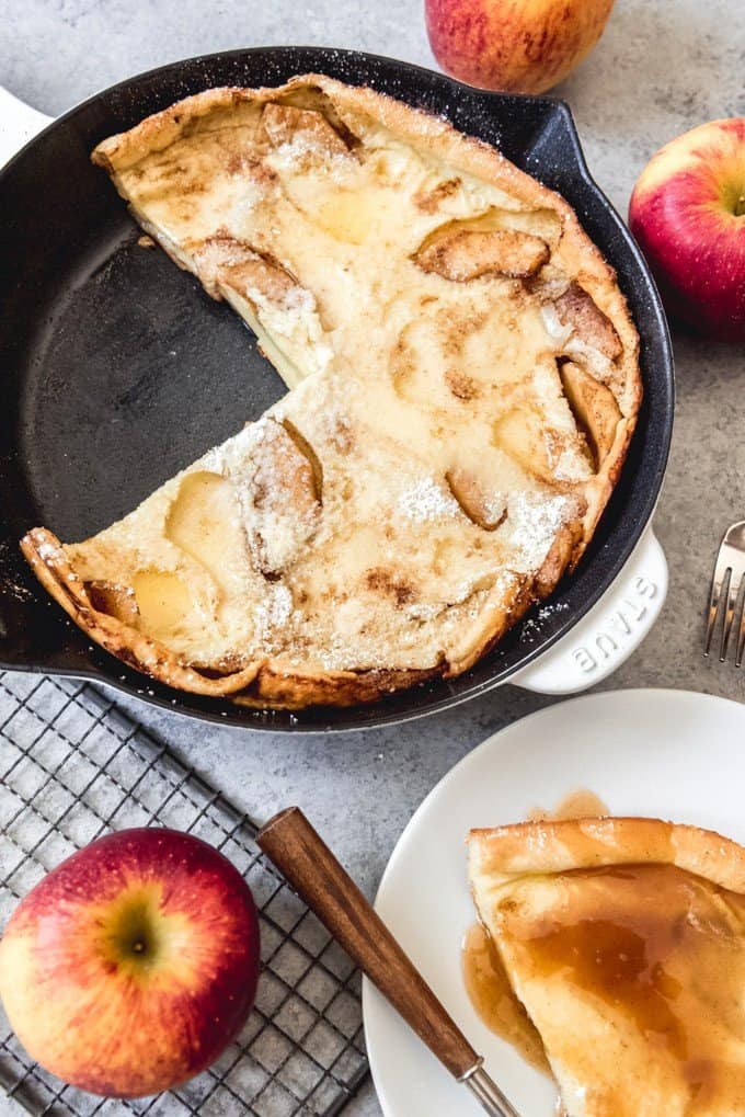 An image of a pan of apple dutch babies with cider syrup with one slice taken out of it.