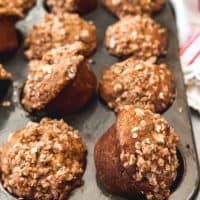 a muffin tin filled with aple oatmeal muffins that are sitting offset and leaning to the sides