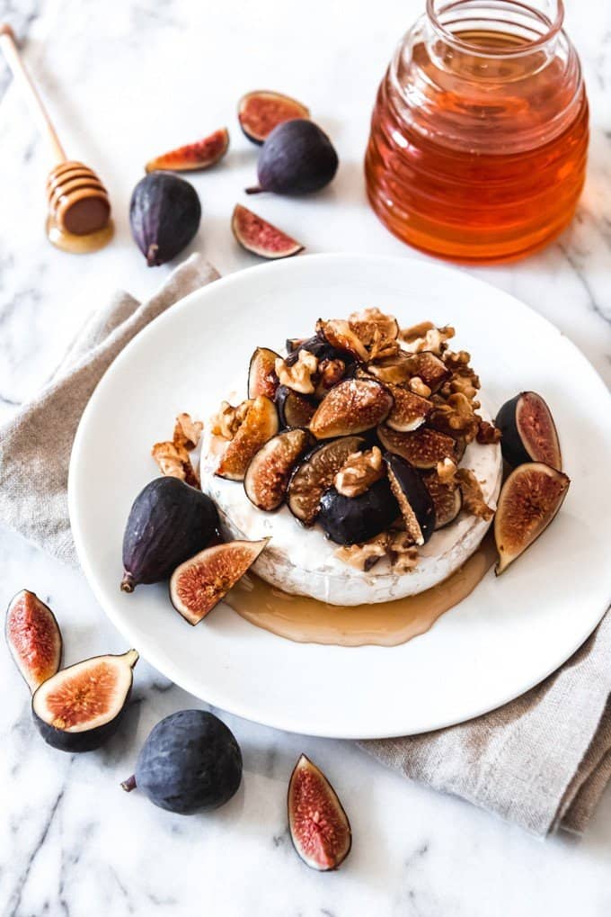 a jar of honey and some fresh figs around a whiteplate with baked brie with walnuts, figs and honey