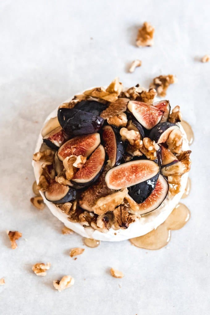 An image of a wheel of brie cheese topped with fresh Mission figs, chopped walnuts, and honey.