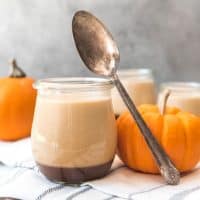 a glass jar filled with pumpkin panna cotta with fresh small pumpkins and a spoon around it