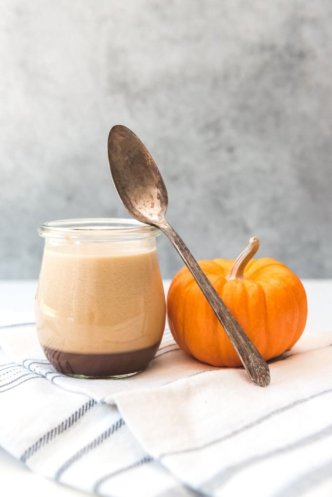 a spoon resting off of the glass jar of caramel panna cotta next to a small pumpkin