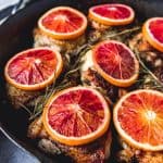blood orange slices on top of cooked chicken thighs with fresh herbs