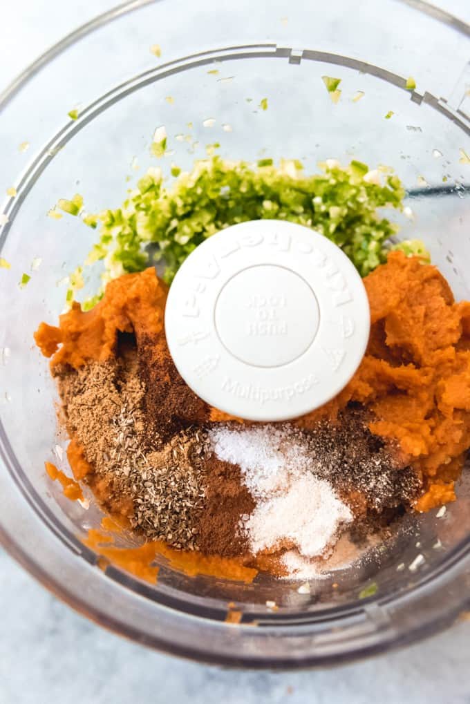 An image of the ingredients for pumpkin enchilada sauce in a food processor.