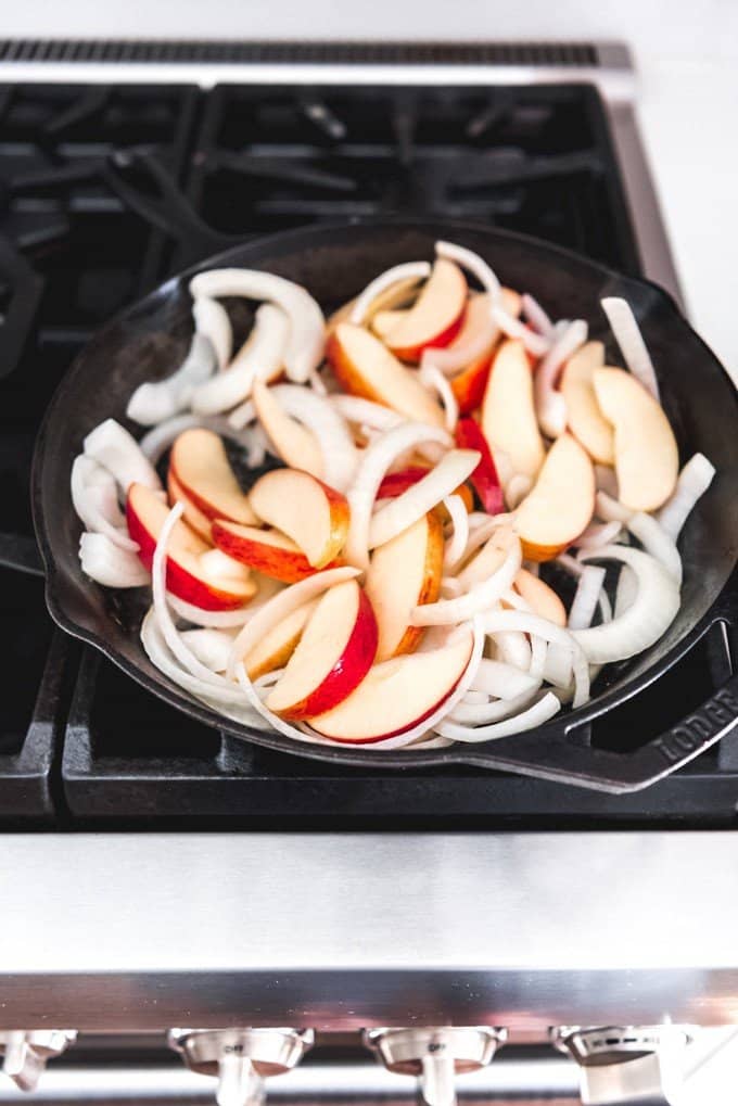 An image of apples and onions in a cast iron skillet on the stove for a chicken skillet meal with apples.