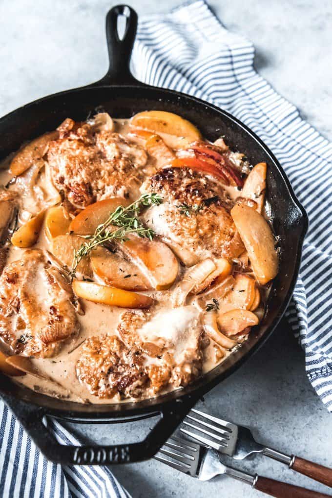 a skillet full of creamy apple cider chicken and topped with fresh herbs for garnish
