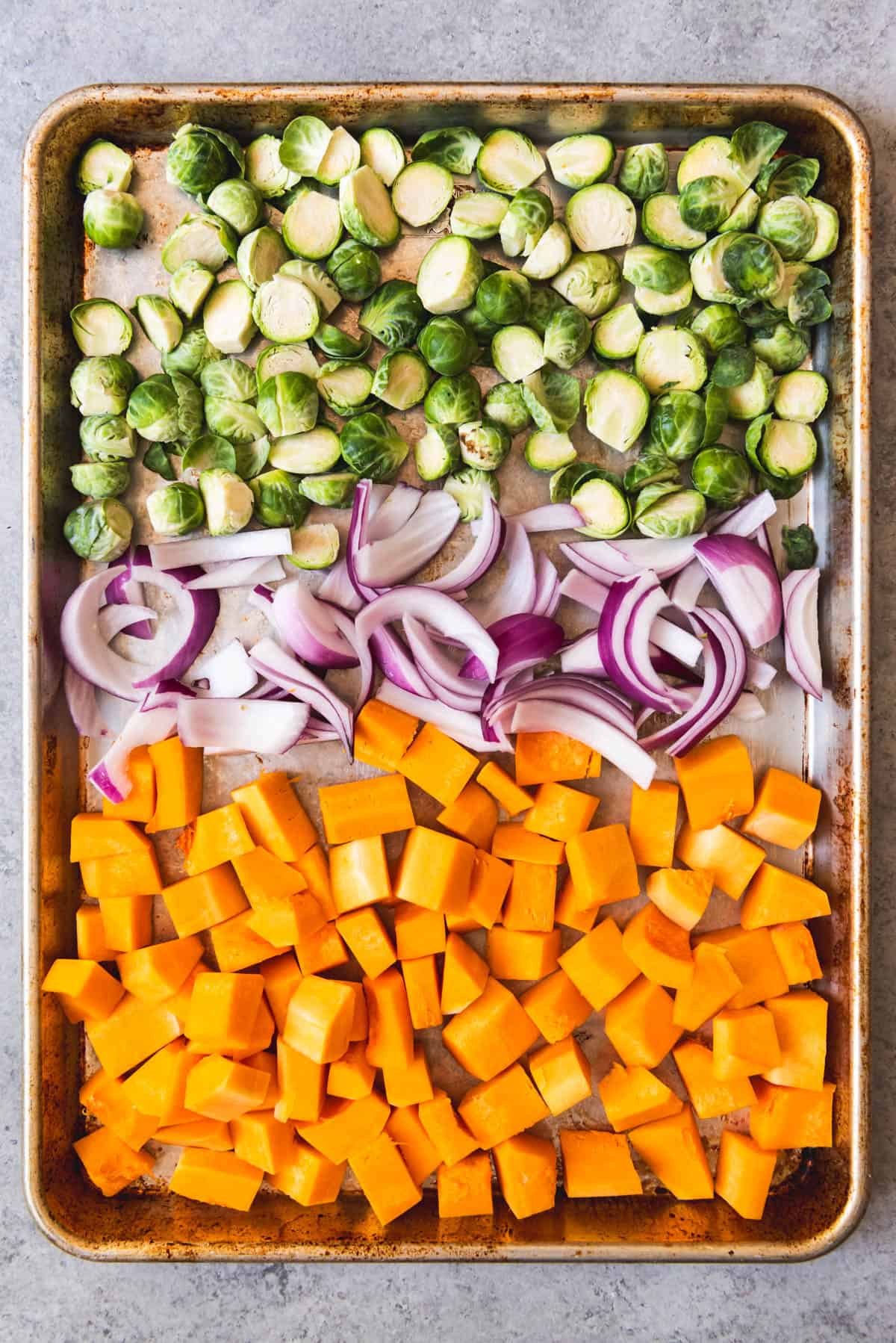 An image of cubed butternut squash, sliced red onion, and brussels sprouts on a baking sheet to be roasted for a delicious Fall salad.