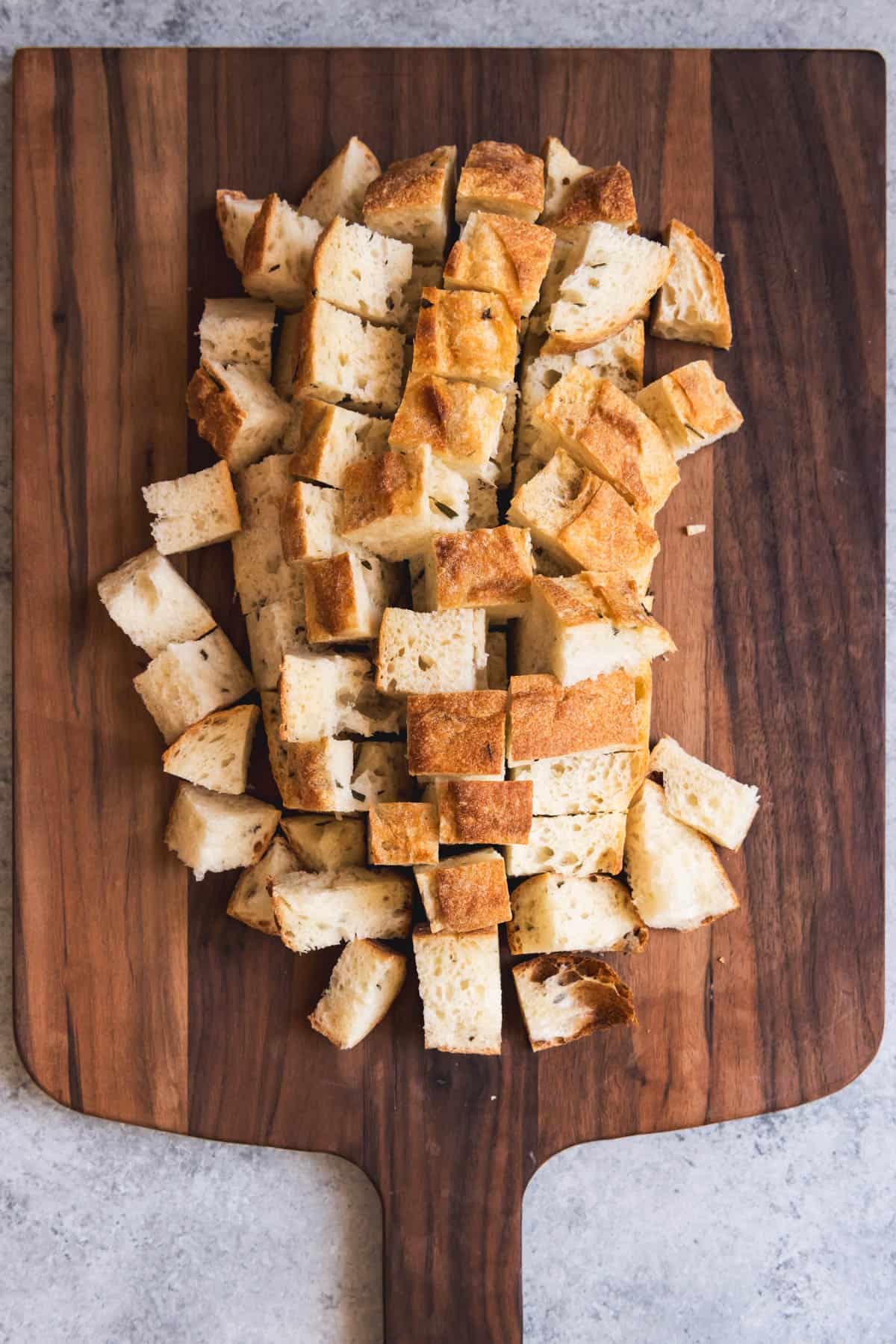 An image of a loaf of crusty bread sliced into cubes before being toasted for a Panzanella bread salad.