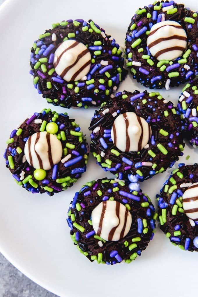 An image of Halloween chocolate sprinkle cookies with white chocolate Hershey's Hugs pressed into the centers arranged on a white plate.