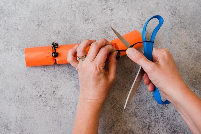 An image of hands using scissors to curl ribbon on Halloween poppers.