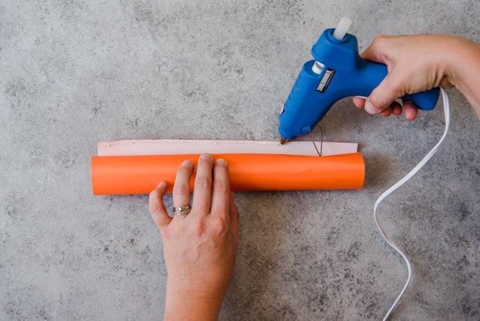 An image of a glue gun running a line of hot glue along wrapping paper to make a homemade Christmas cracker in a step-by-step photo tutorial.