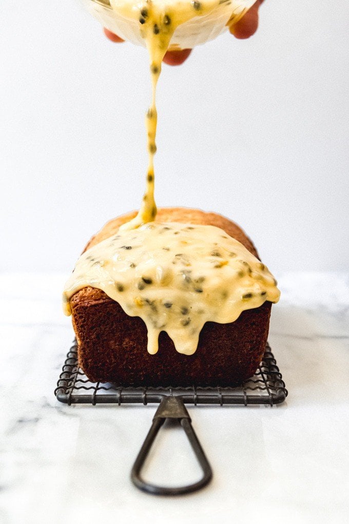 An image of passion fruit glaze being drizzled over a fresh lemon loaf cake.