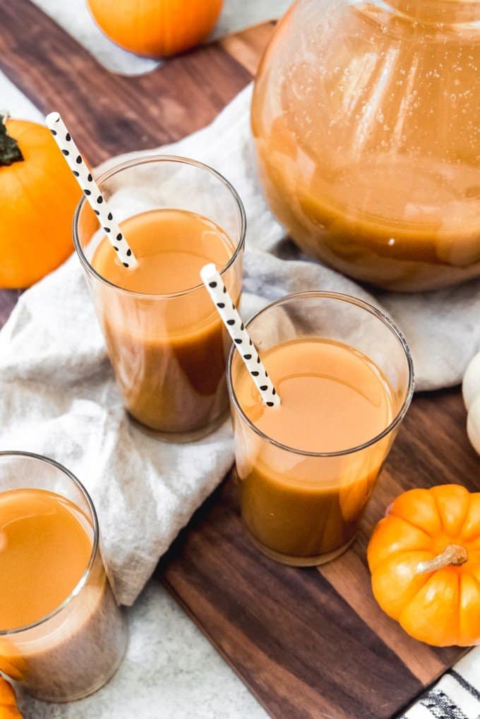 An image of two glasses of cold pumpkin juice with a pitcher of pumpkin juice next to them.