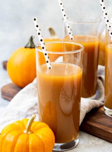 Tall glasses filled with pumpkin juice with spotted straws inside and pumpkins scattered around.
