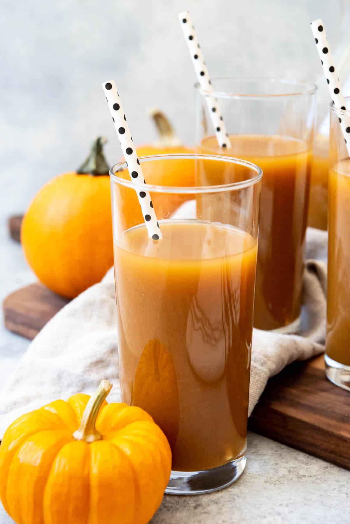 Tall glasses filled with pumpkin juice with spotted straws inside and pumpkins scattered around.