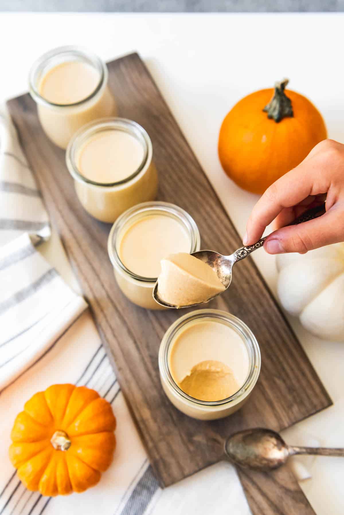 An overhead image of a spoon lifting a bite of pumpkin panna cotta from a jar.