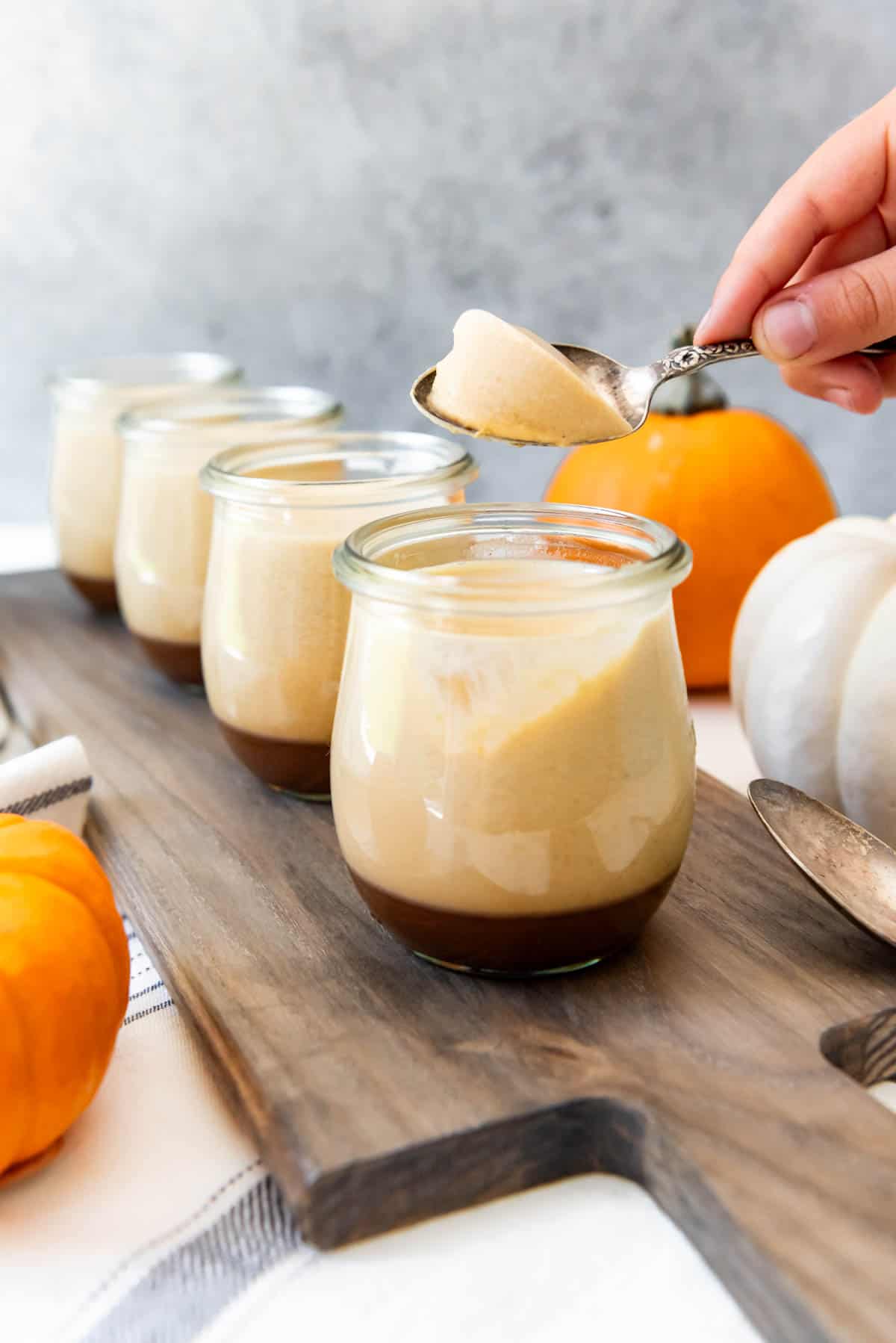 An image of a hand holding a spoon with a scoop of salted caramel pumpkin panna cotta from an individual dessert cup.