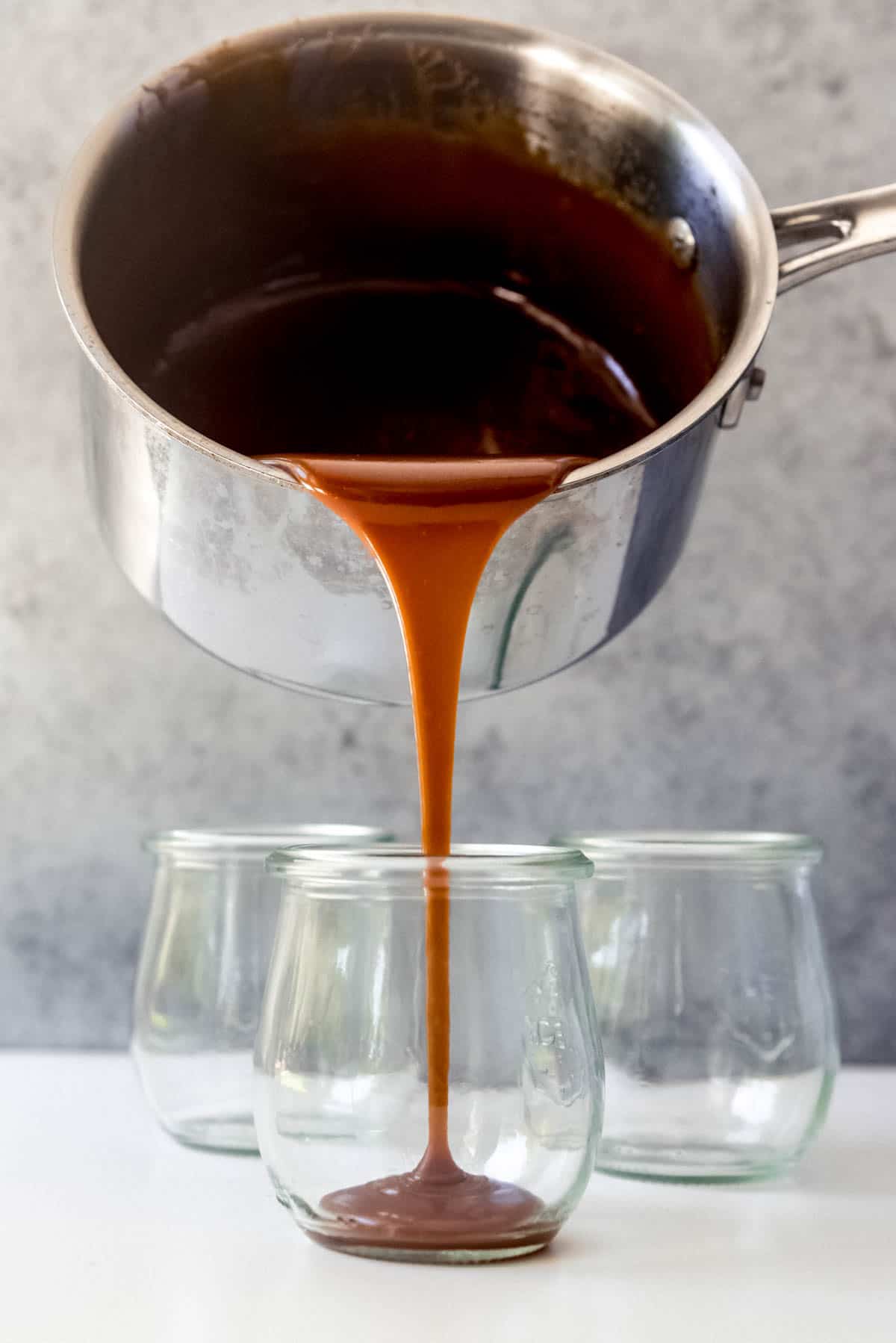 An image of salted caramel sauce pouring from a pan into glass jars for a pumpkin panna cotta with caramel sauce.