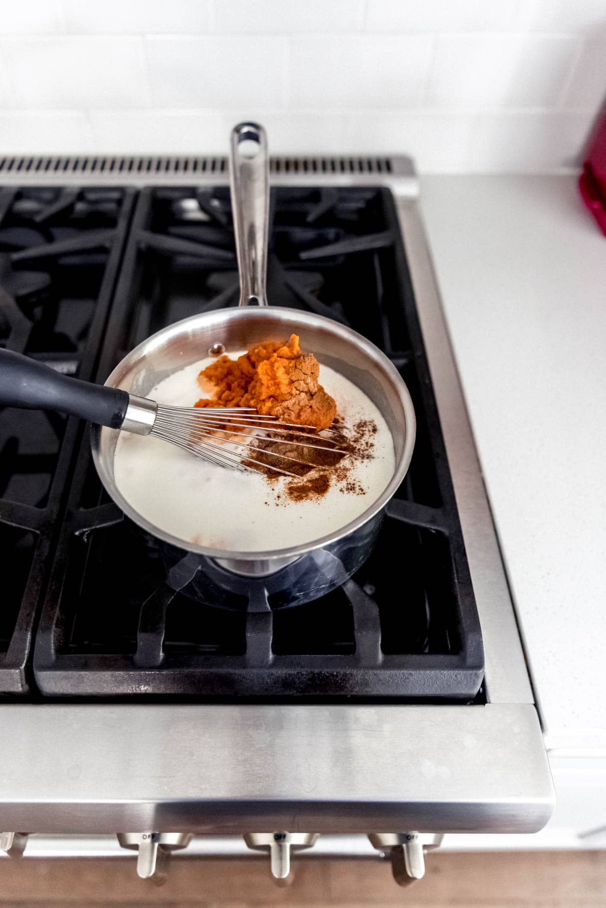 An image of cooked cream and whole milk in a saucepan on the stove with sugar, pumpkin puree, cinnamon, and other spices for a pumpkin panna cotta recipe.