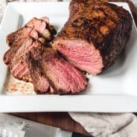 tri tip sliced on a white plate with a knife to the side