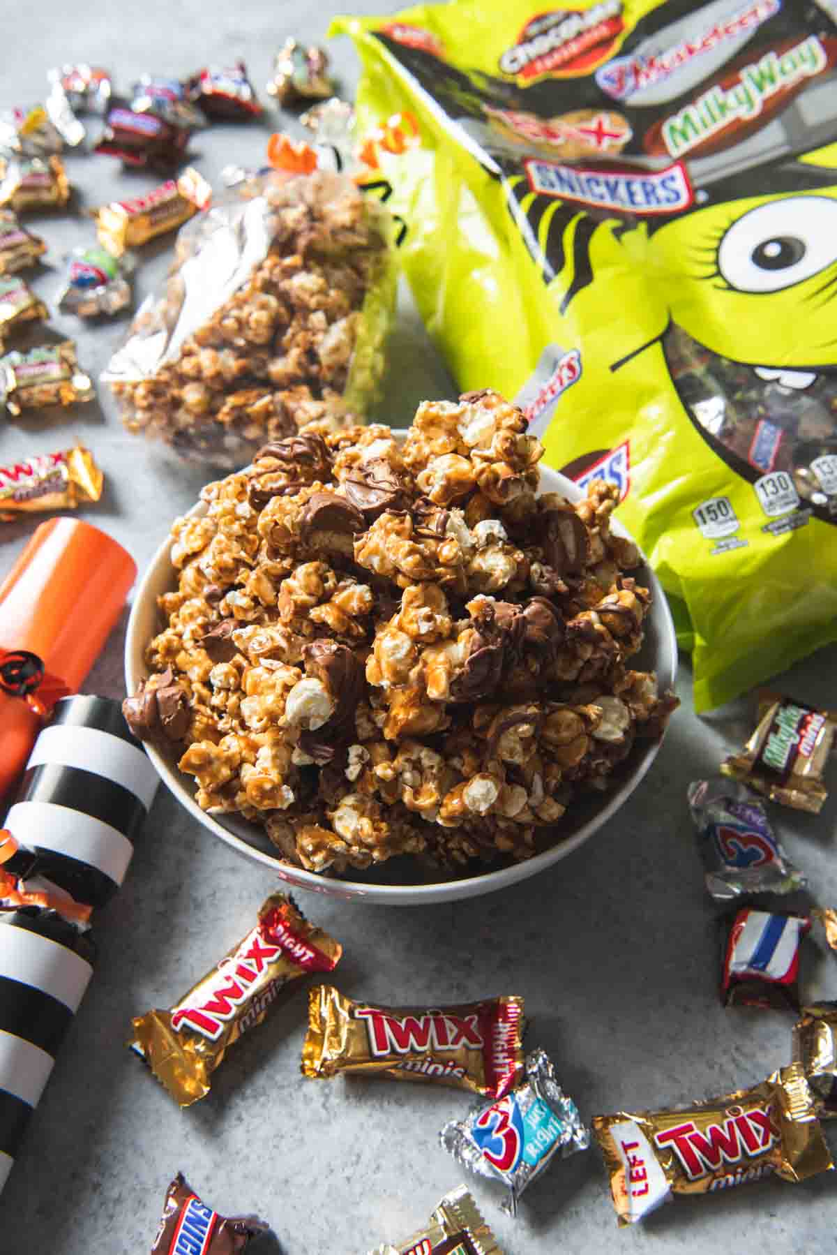 A white bowl of Twix caramel popcorn surrounded by candy.