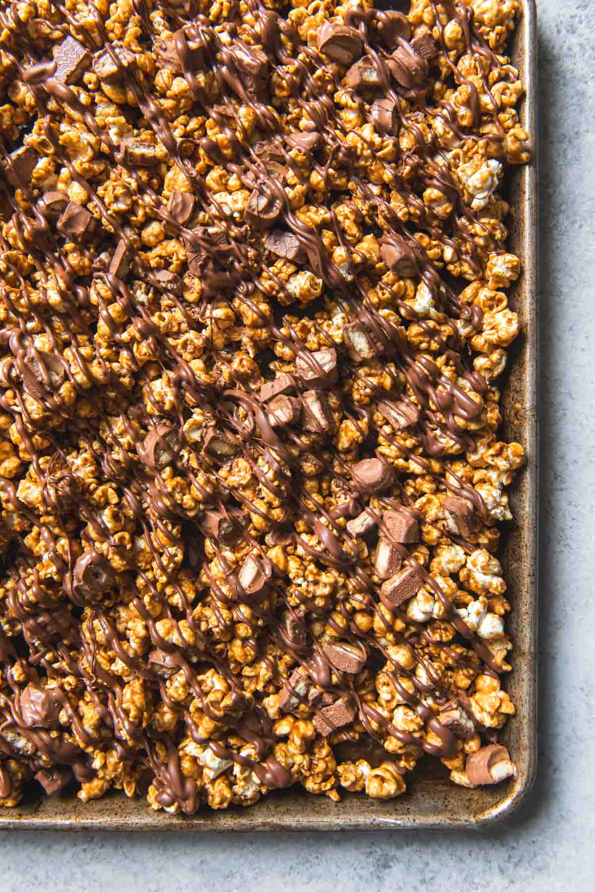 An image of a baking sheet full of homemade Twix caramel popcorn drizzled with melted chocolate.