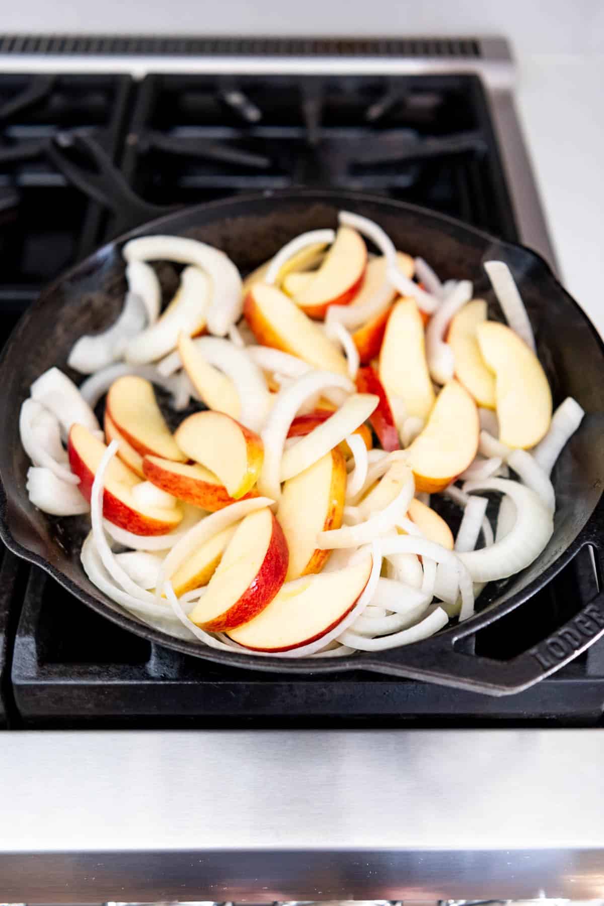 An image of apples and onions in a cast iron skillet on the stove for a chicken skillet meal with apples.