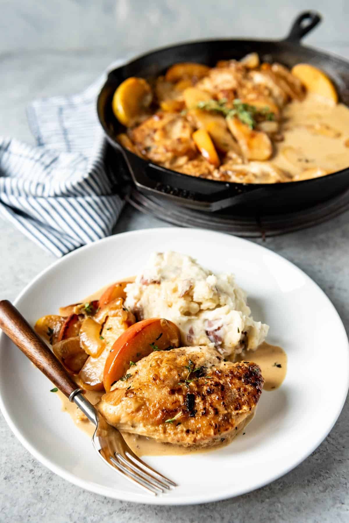 An image of a plate of pan seared chicken with apples and onions with mashed potatoes on the side.