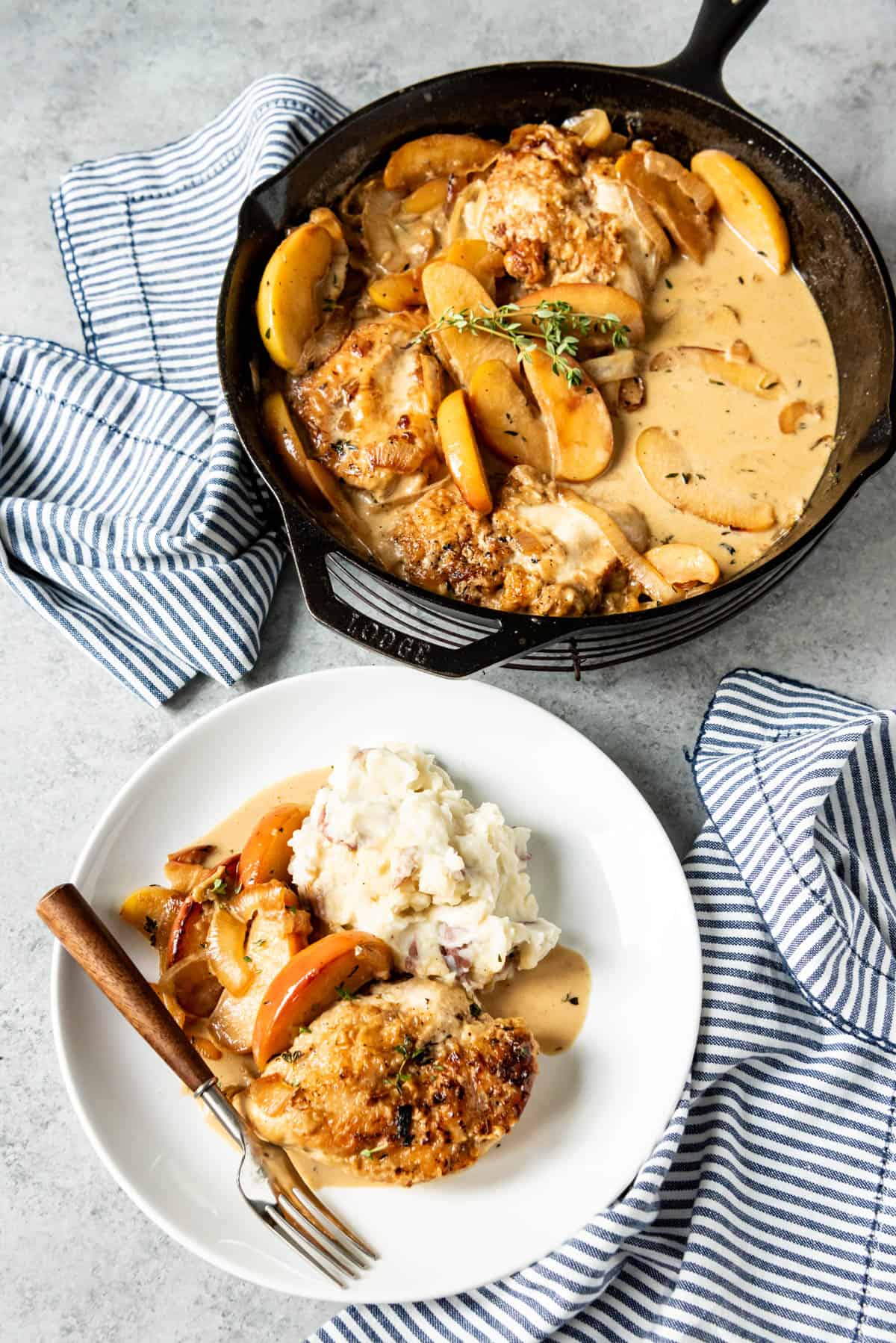 An image of a plate of pan seared chicken with apples and onions with mashed potatoes on the side.