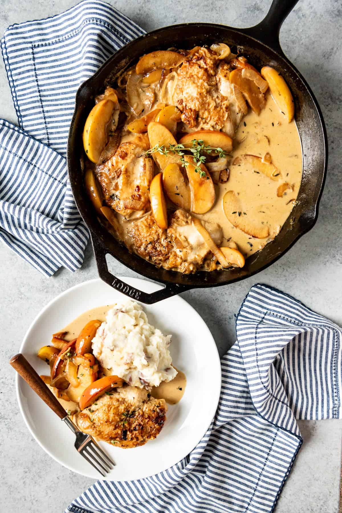 A plate of chicken, apples, onions, and potatoes next to a skillet of cooked chicken and apples.