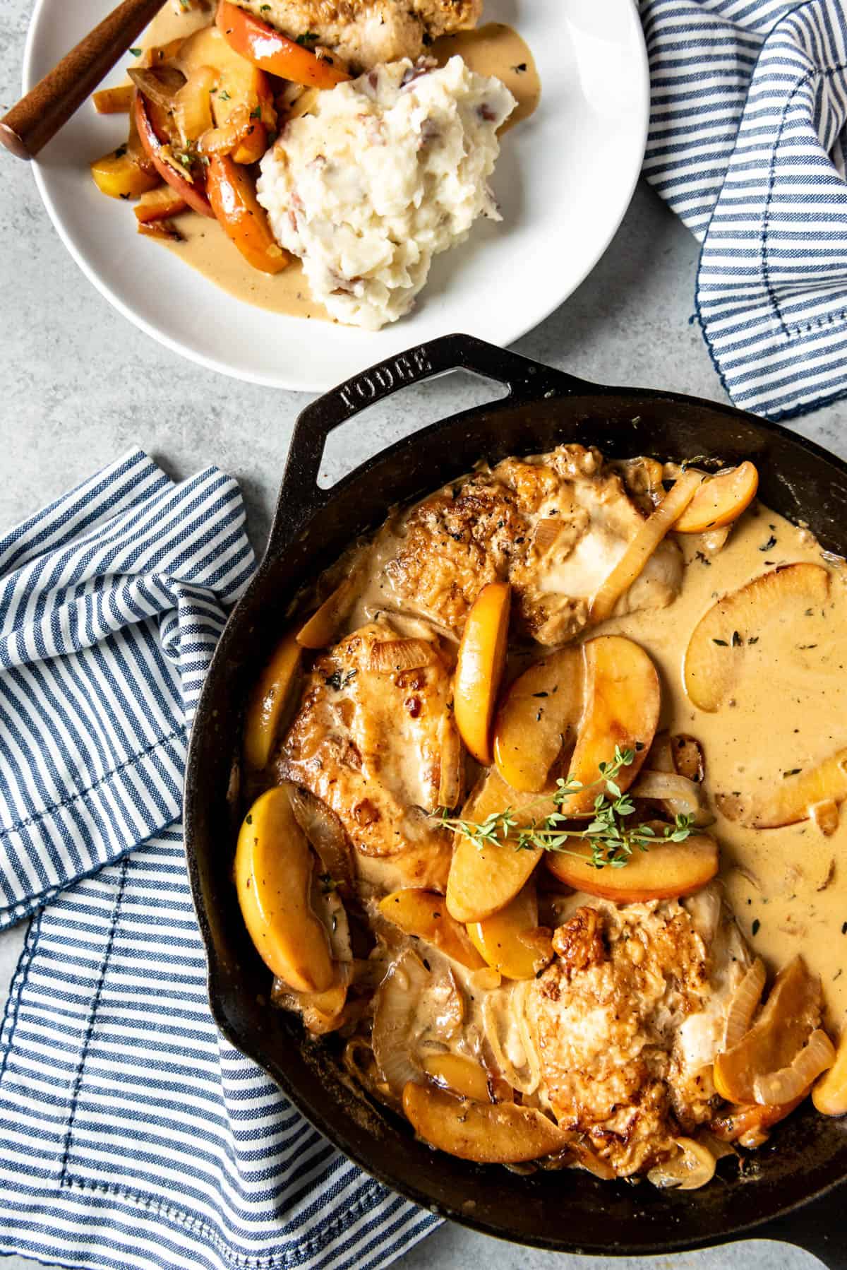 An overhead image of chicken, apples, and onions in a large skillet.